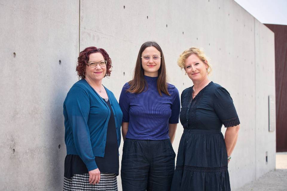 Three women stand in front of a stone wall