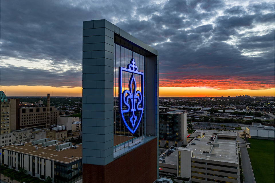 The SLU logo at the top of a building on campus at sunset.