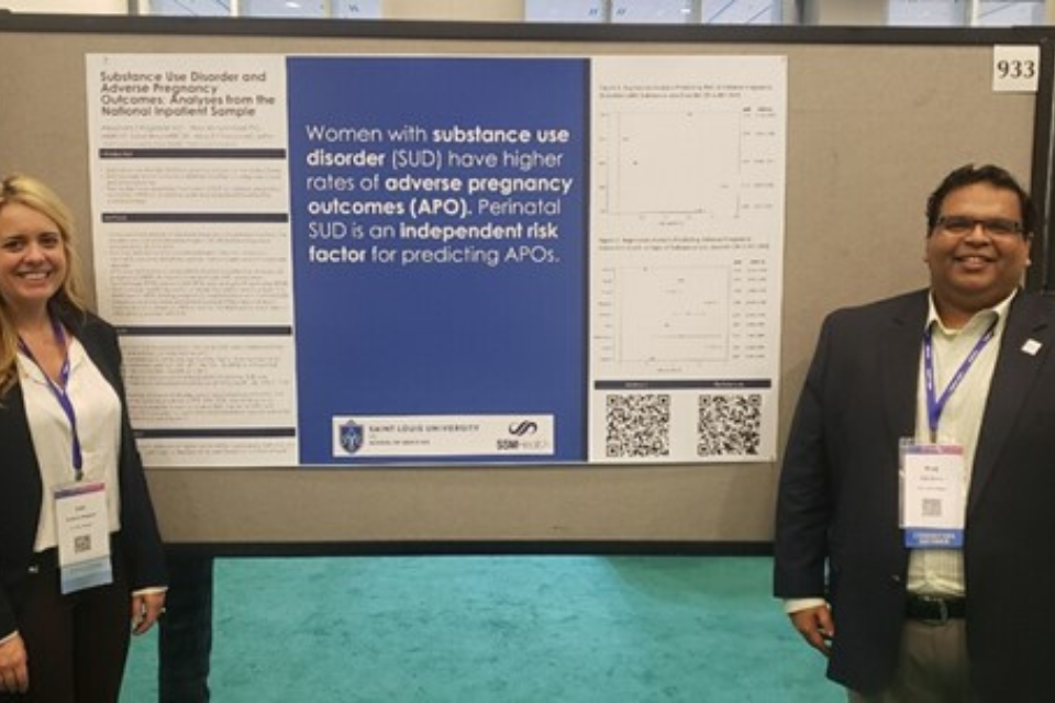 Fellows research Two students stand in front of a research poster at an event.