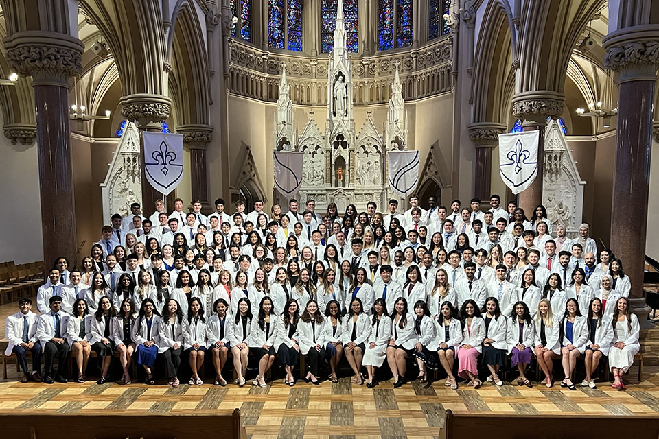 Medical students wearing white coats pose for a photo inside a church.