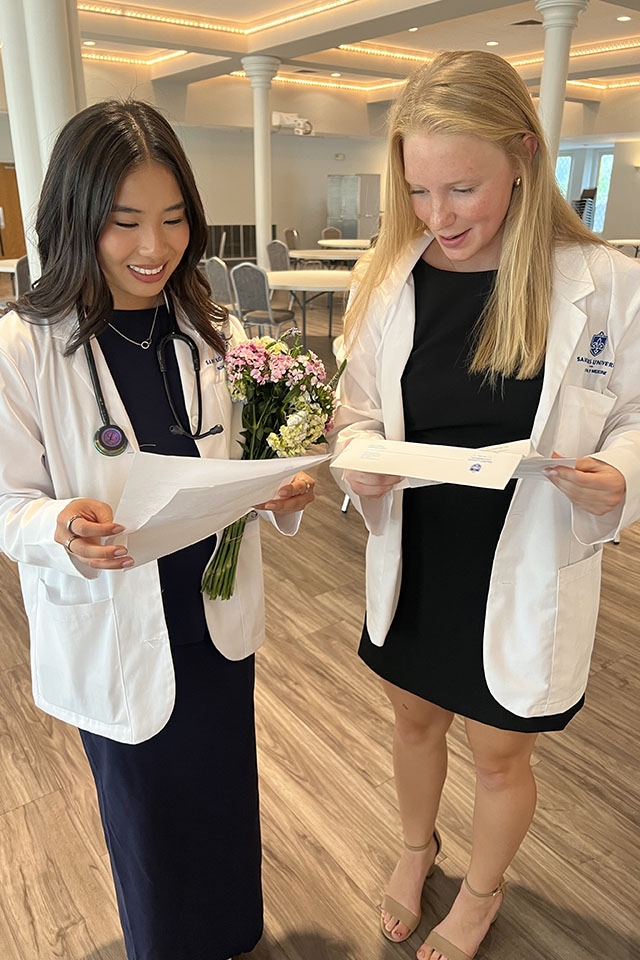Two female medical students excitedly read notes of encouragement from alumni.