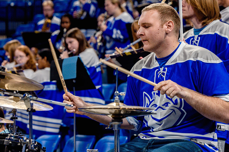 A blonde man in a blue-and-white hockey jersey drums.