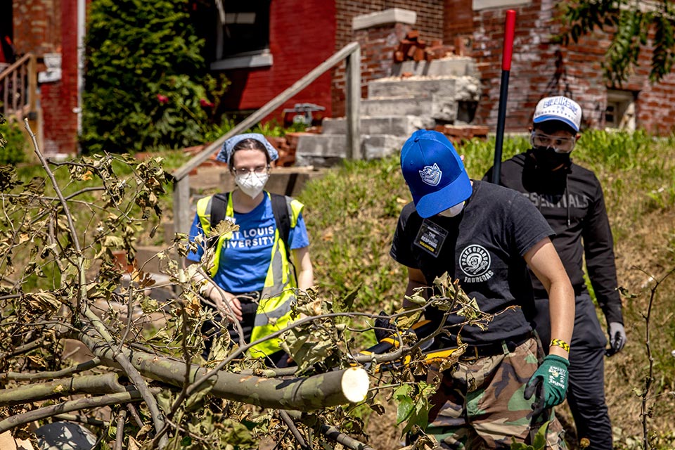Alumni in safety gear walk down a St. Louis street picking up branches
